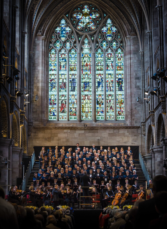 Festival chorus in front of Hereford Cathedral stain glass window